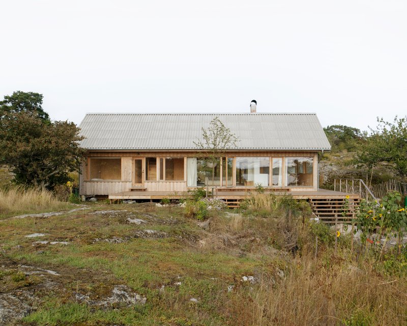 Timber cottage with corrugated metal roof and wraparound deck set among rocky outcrops and grasses