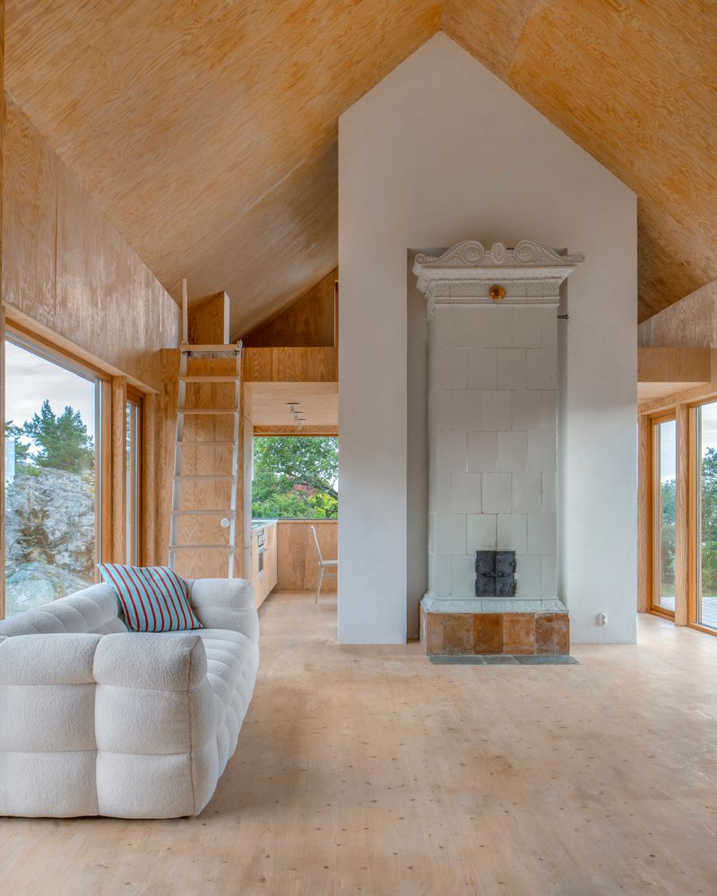 White masonry stove chimney rising through plywood lined interior with vaulted ceiling and loft ladder