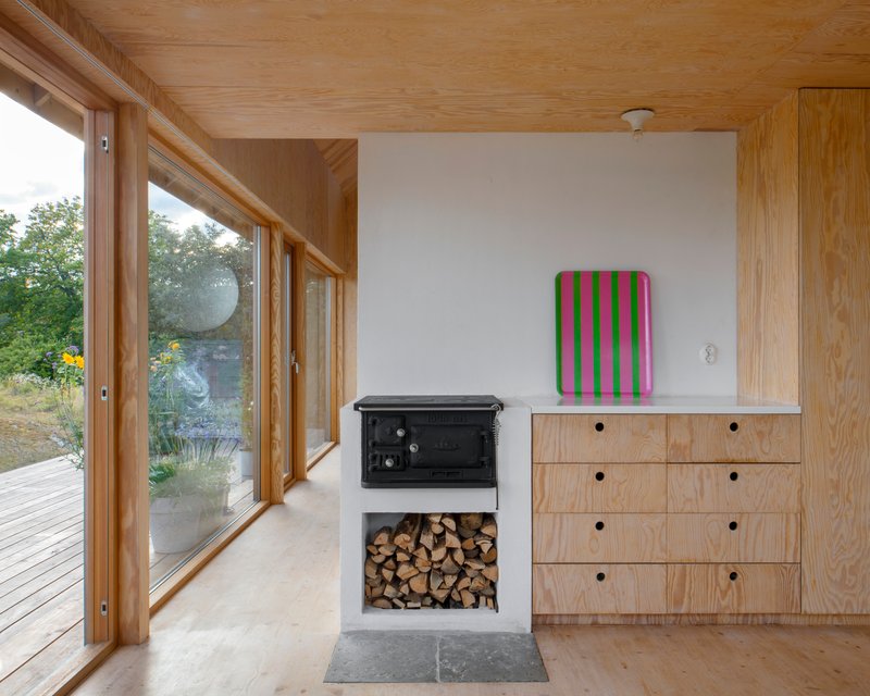 Cast iron wood stove with firewood storage niche beside plywood cabinetry under a timber ceiling