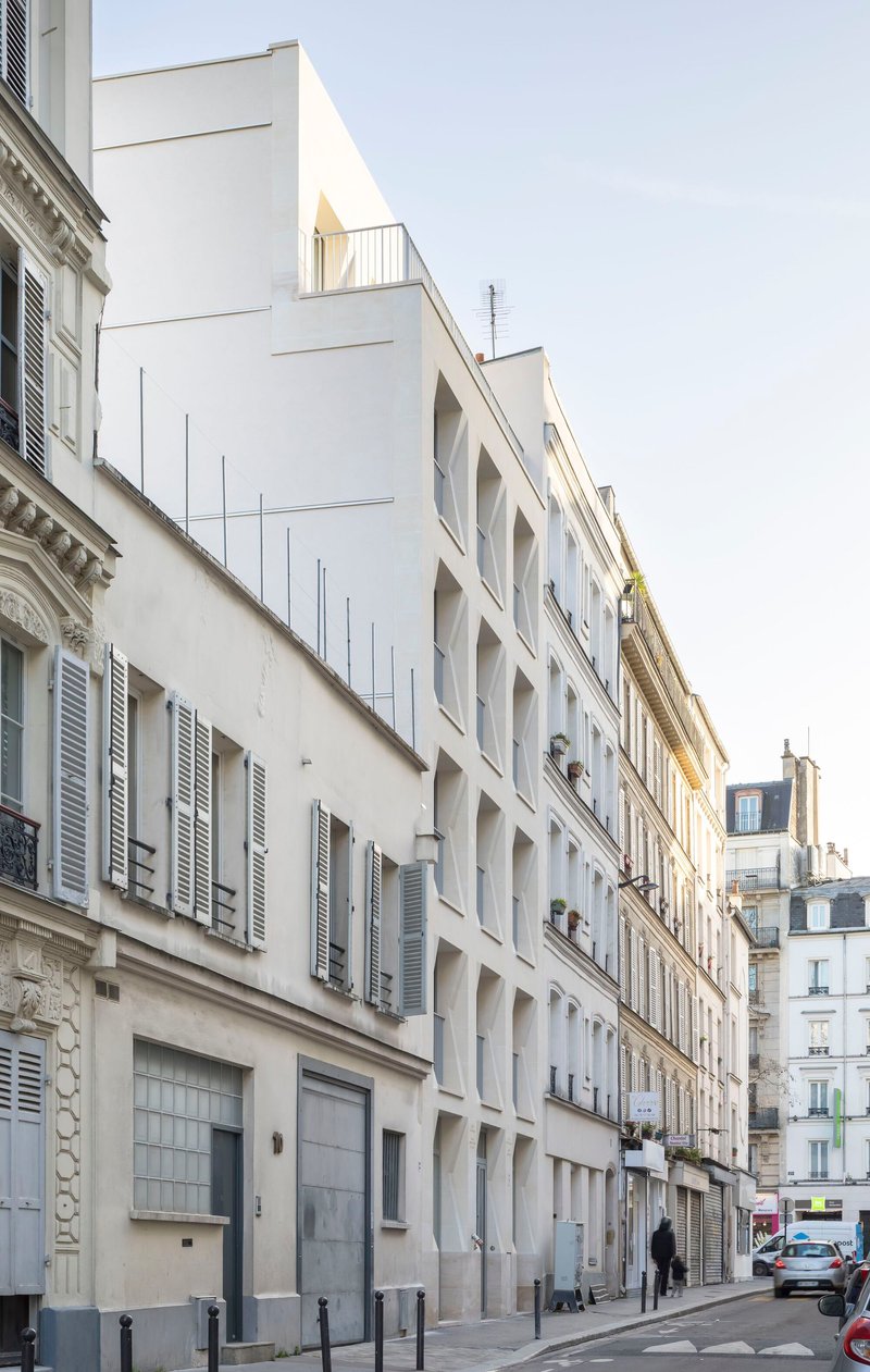 Street view of white residential facade with deep window reveals between ornate heritage buildings
