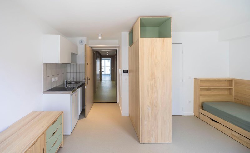 Studio interior with timber wardrobe, bed platform, kitchenette and pale resin flooring