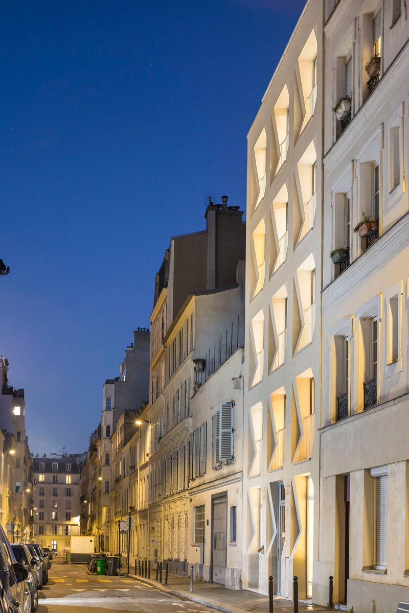 Illuminated facade at dusk showing deep window recesses glowing along narrow street