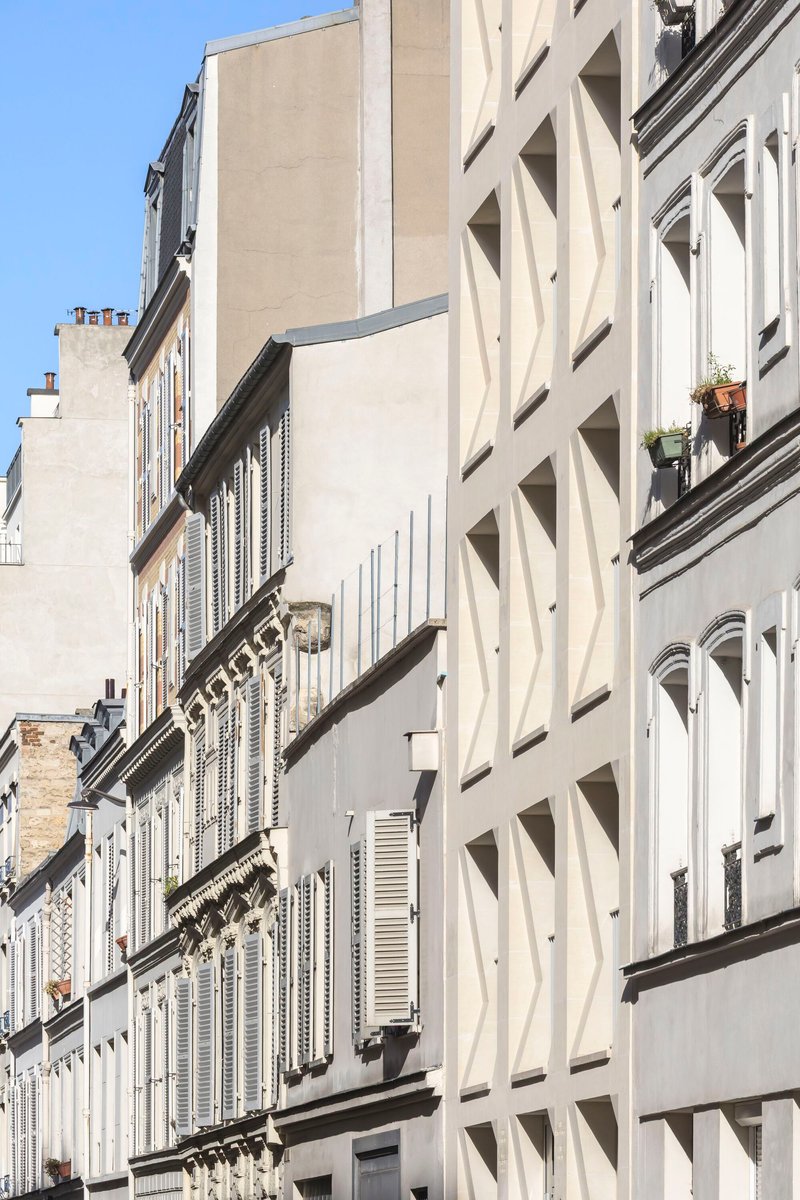 Street view of the faceted white facade alongside neighboring buildings with shuttered windows