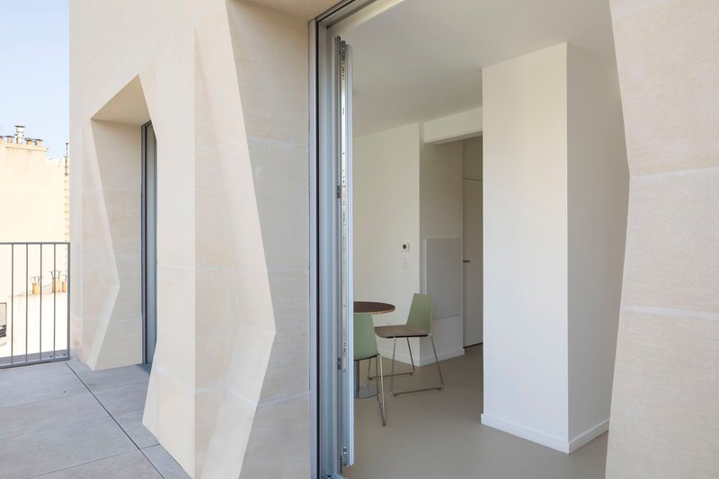 Interior threshold opening from terrace through angular white reveals to dining space beyond