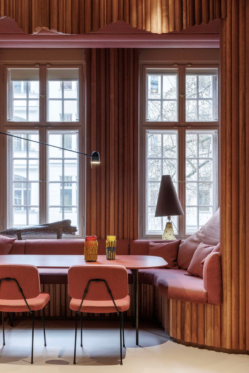 Window banquette with fluted timber cladding, pink cushions, and wall-mounted pendant lamps overlooking winter trees