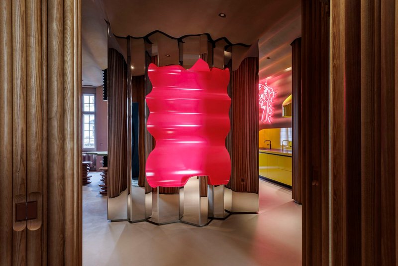 Pink inflatable sculpture on zigzag metal base within timber-clad hallway with views to adjacent rooms