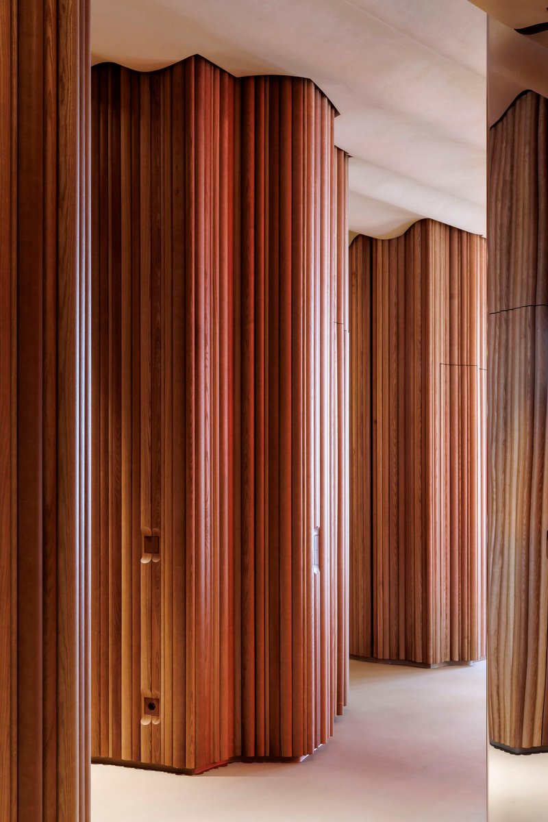 Curved vertical fluted timber wall panels in varying wood tones forming corridor with white ceiling
