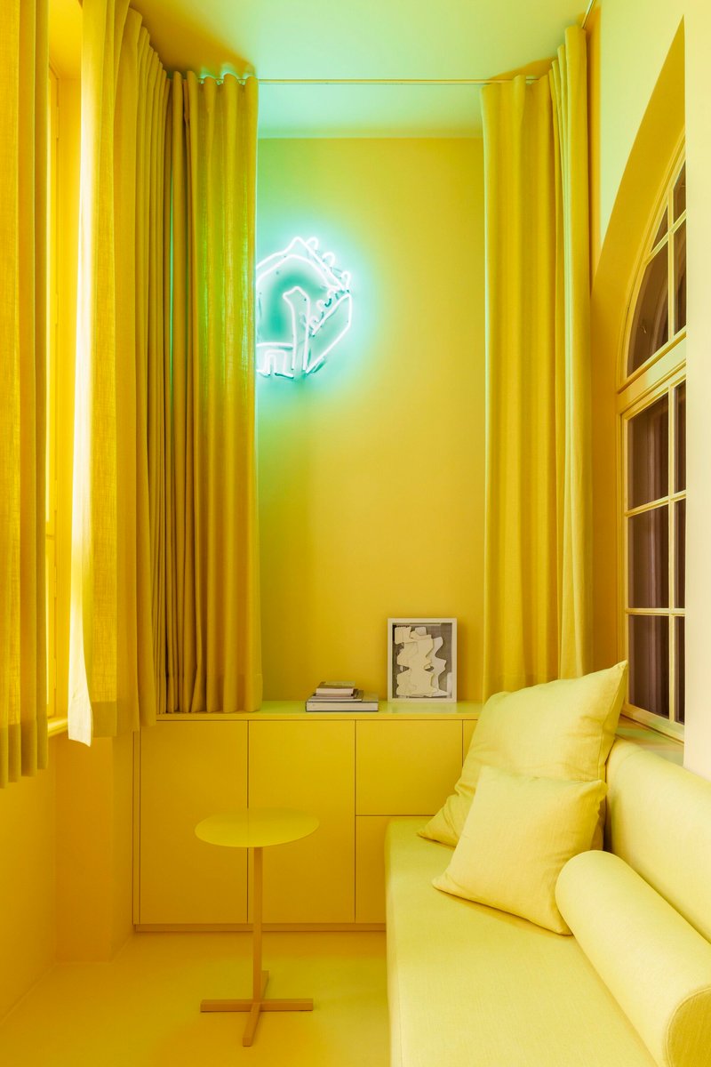 Yellow sitting room with floor-to-ceiling curtains and a neon artwork casting green and yellow light