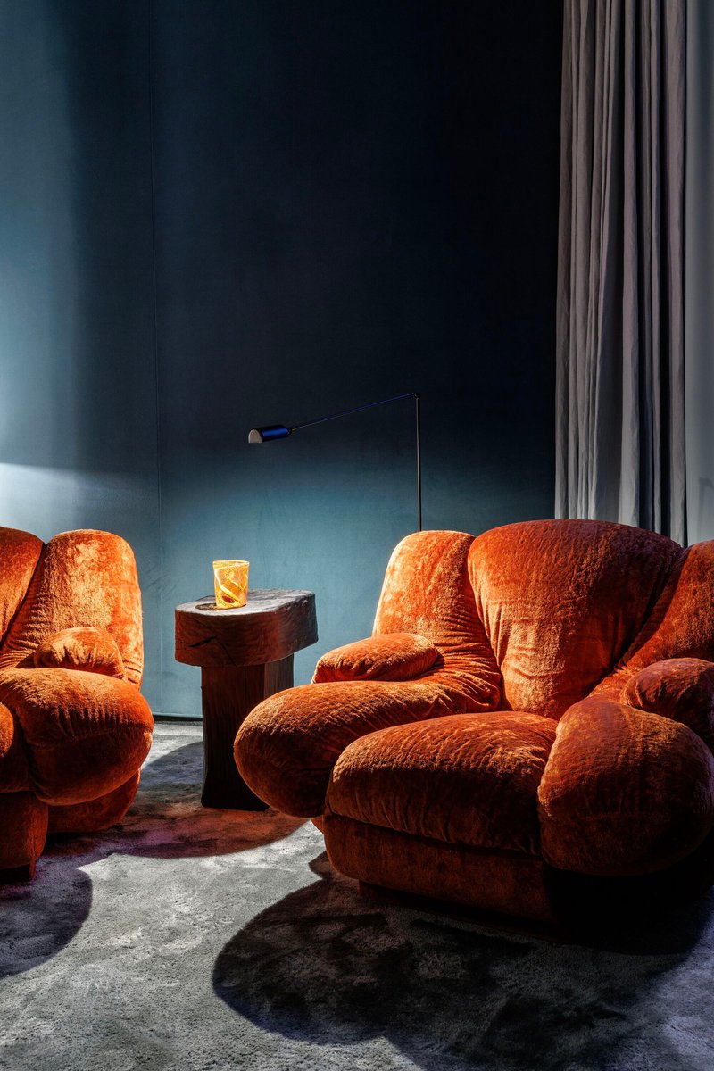 Lounge corner with rust-colored velvet chairs grouped around a cylindrical timber side table