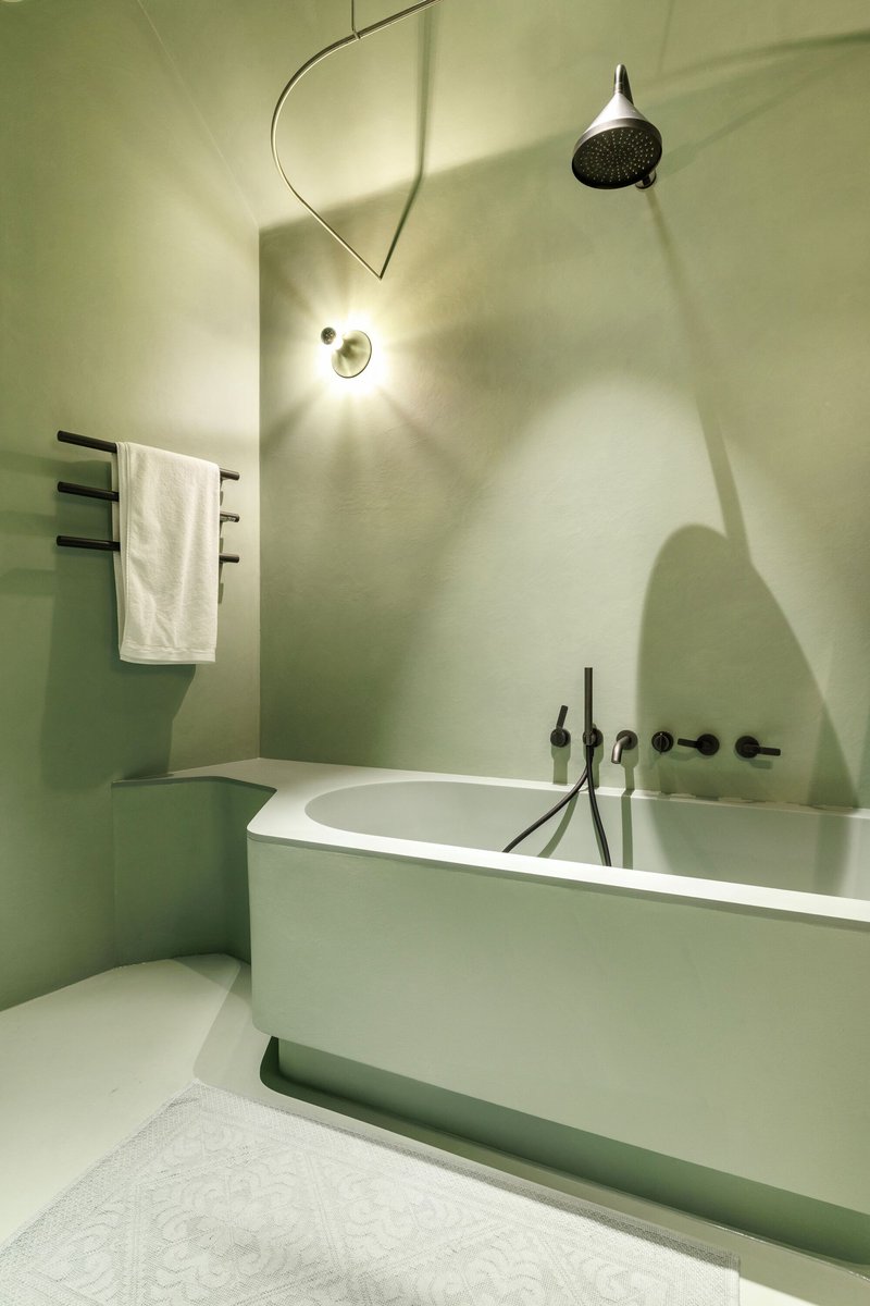 Bathroom with white freestanding tub and curved arc shower fitting against pale green plastered walls
