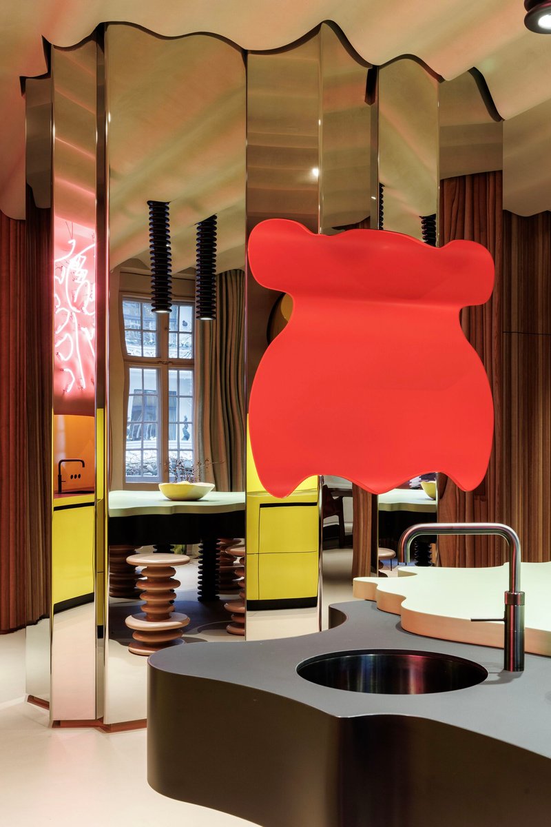 Kitchen island with integrated sink beneath a large coral-colored pendant sculpture and mirrored partition