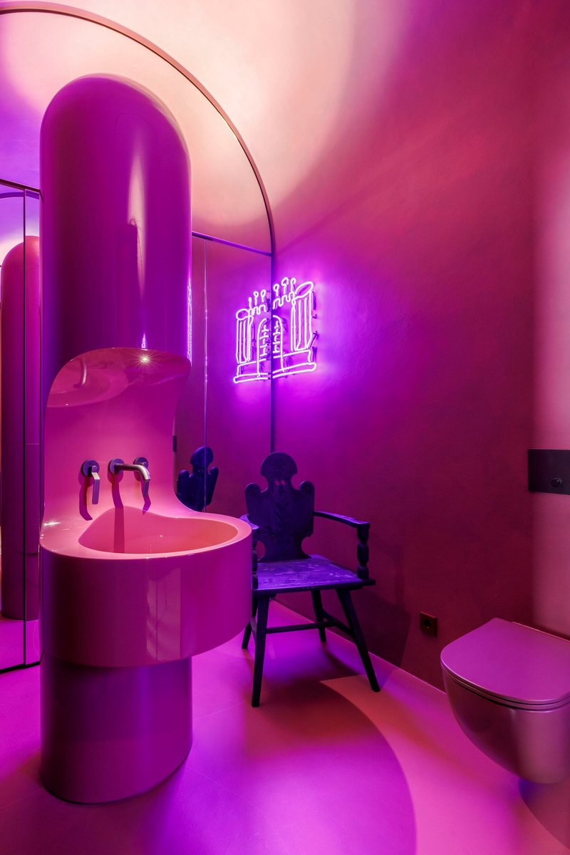 Bathroom with pink cylindrical sink and purple neon lighting illuminating vaulted ceiling and arched doorway
