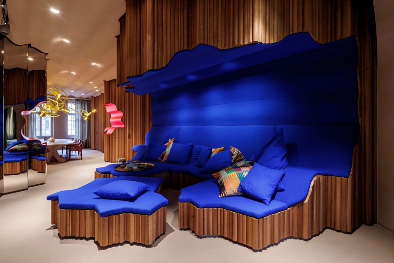 Cobalt blue upholstered seating with undulating headboard and fluted timber base against vertical wood paneling