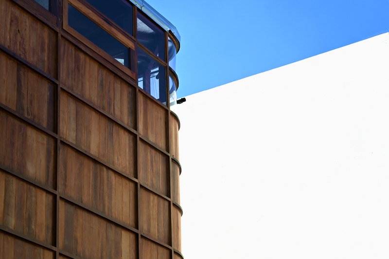 Junction of the cylindrical timber-clad volume with glazed upper level and white rendered wall