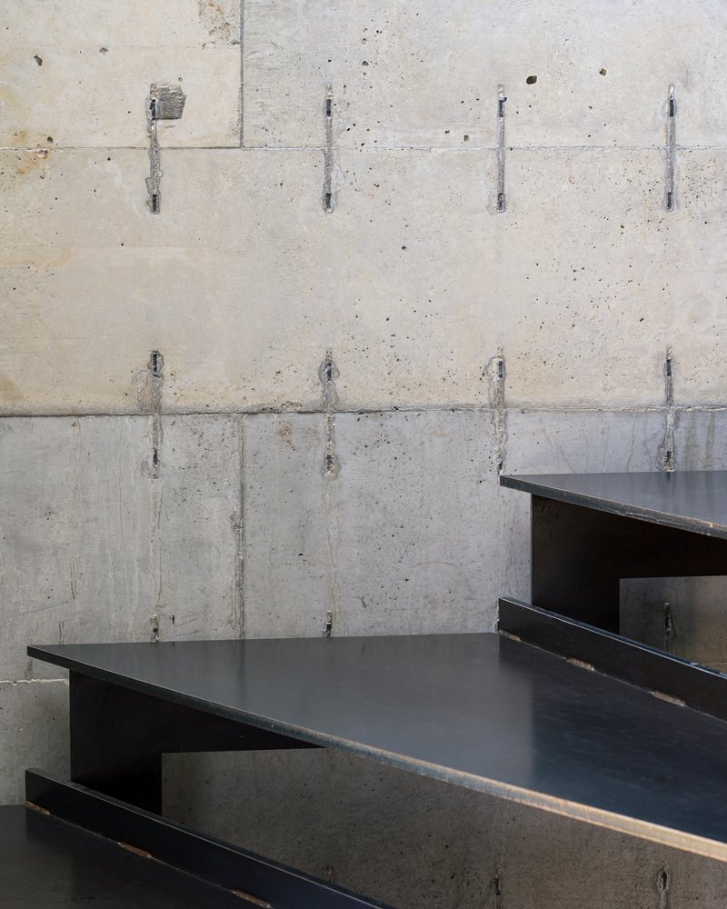Close-up of steel stair treads cantilevered from board-formed concrete wall with tie holes