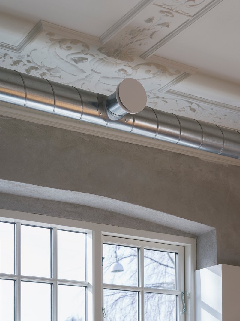 Exposed spiral ductwork running below decorative white ceiling molding near gridded windows