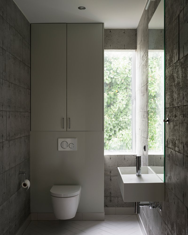 Bathroom with wall-hung basin, tall storage cabinet, and window overlooking green foliage outside
