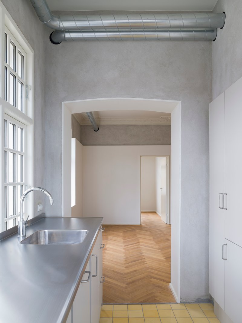 Kitchen with stainless steel counter and yellow tile floor opening to herringbone wood flooring beyond