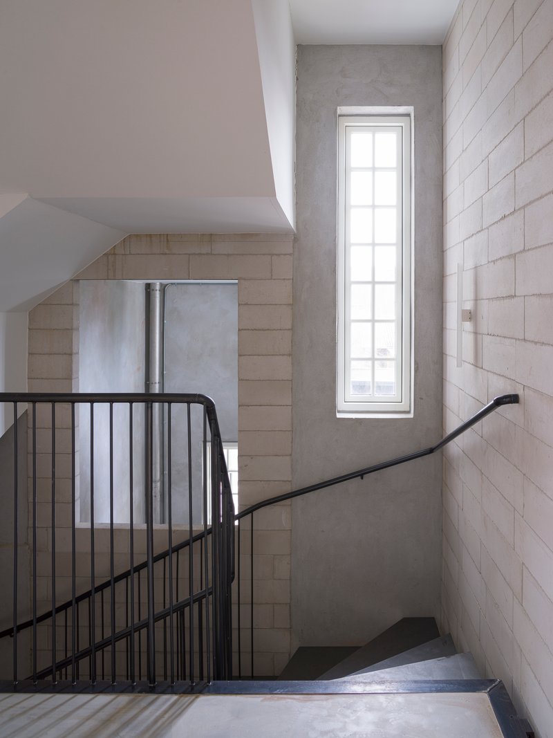 Stairwell with black metal railing and tall vertical window illuminating concrete block walls