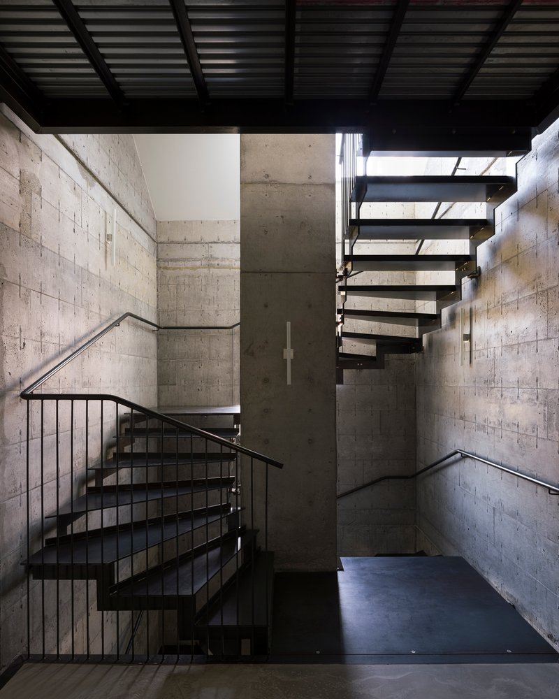 Double-height stairwell with exposed concrete block walls and black steel open-riser stairs under skylights