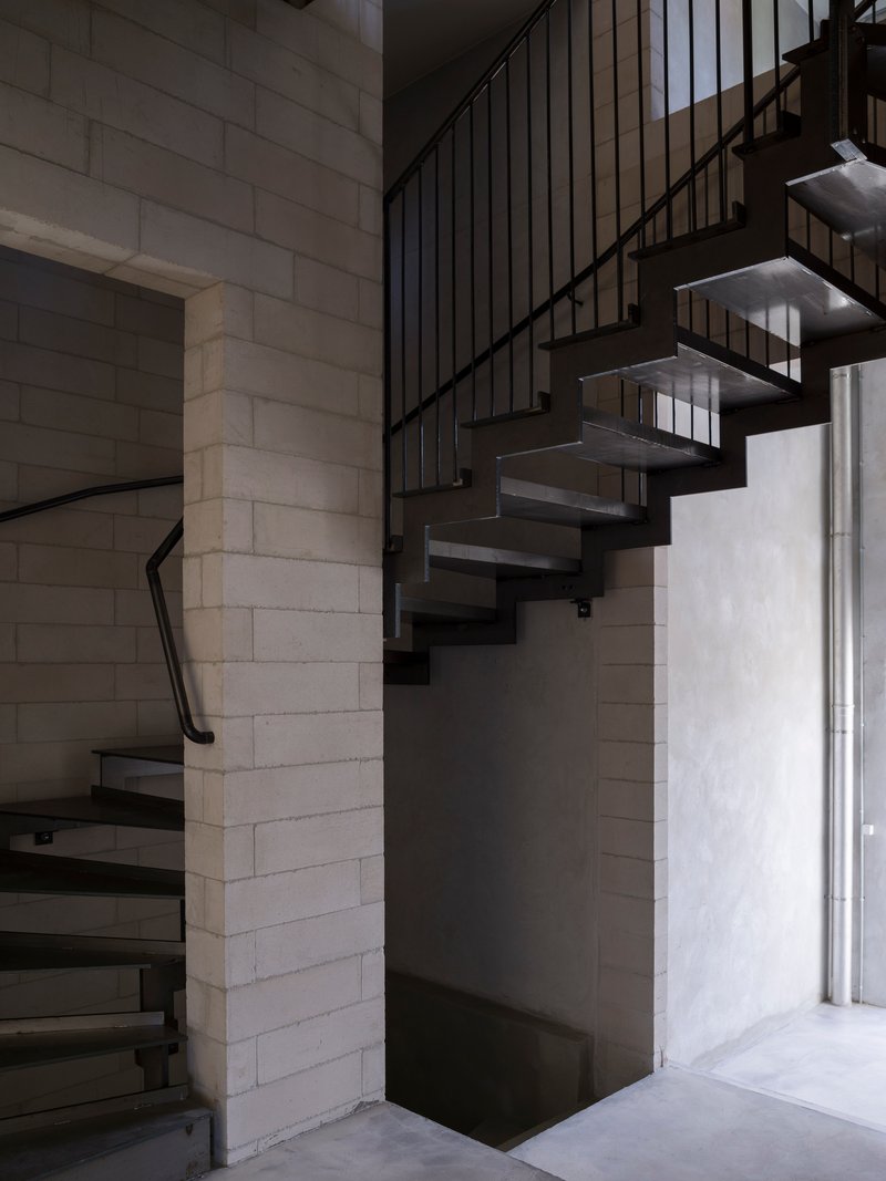 Steel open-tread staircase winding between concrete block walls with vertical metal railing