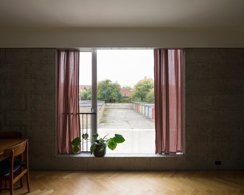 Wide window with pink curtains framing a view of a concrete terrace and distant trees
