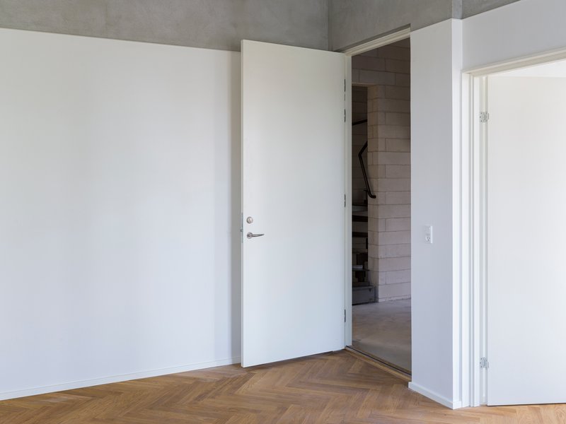 White door slightly ajar revealing a glimpse of the concrete block hallway beyond herringbone flooring