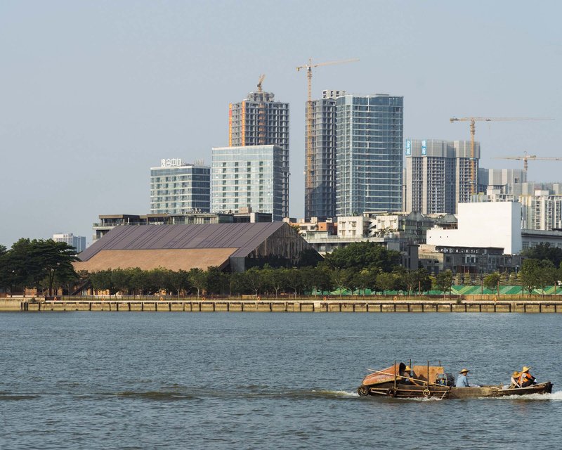 Waterfront view of the timber-clad roof structure against highrise towers under construction