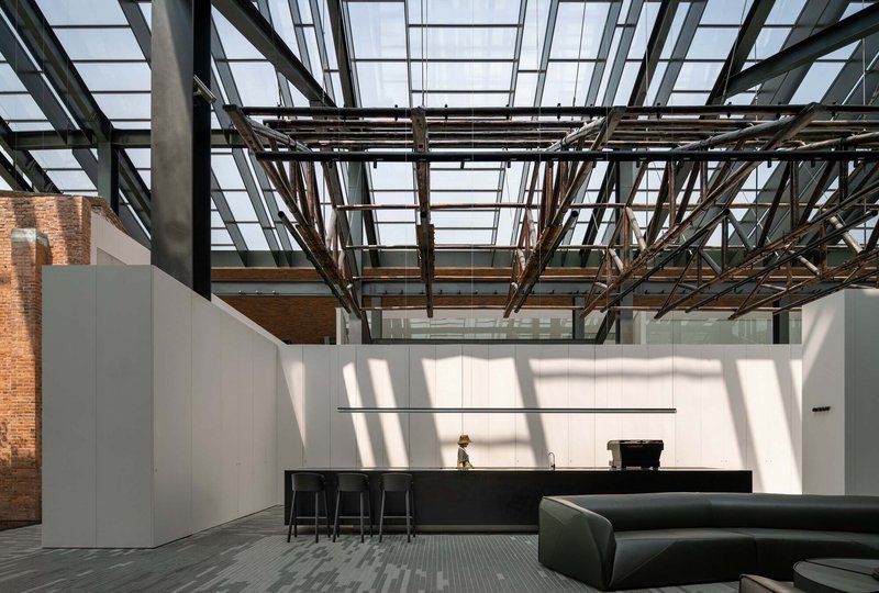 Interior space with exposed steel truss ceiling and glazed roof casting geometric shadows across white walls