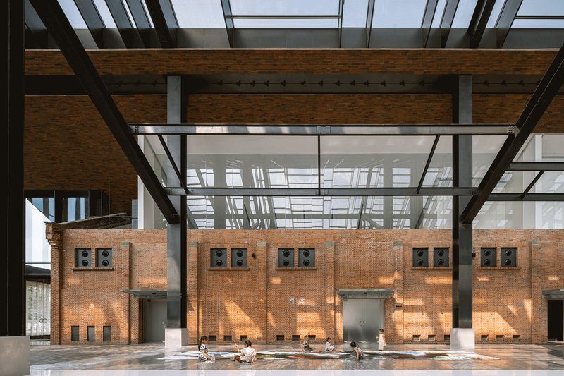 Interior view of retained brick wall with steel openings under a glass and steel trussed roof