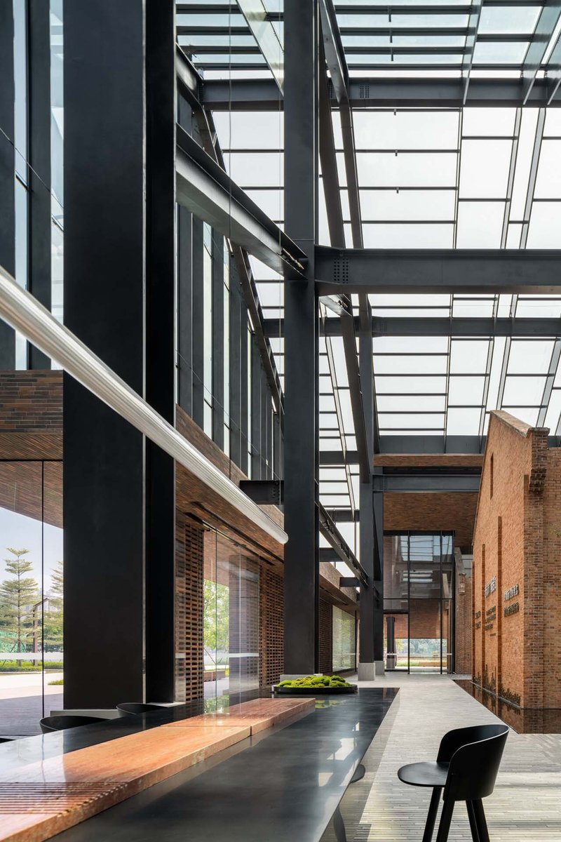 Atrium corridor with black steel structure and glazed roof above timber benches and planted beds