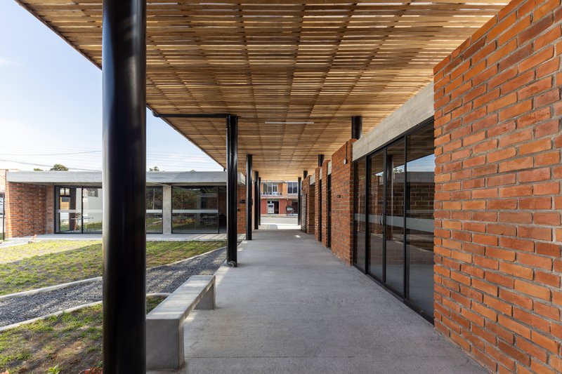 Covered exterior corridor with slatted timber ceiling, black columns, and concrete bench along brick wall