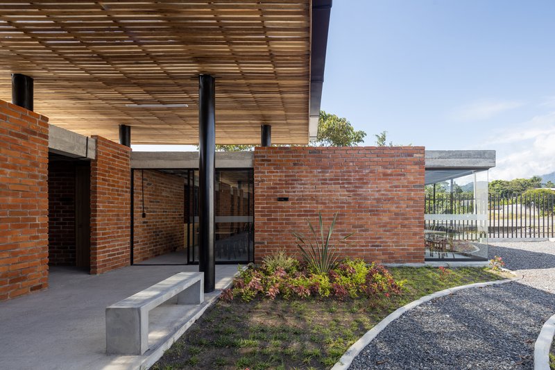 Entrance courtyard with red brick walls, timber slatted canopy, concrete bench and planted bed