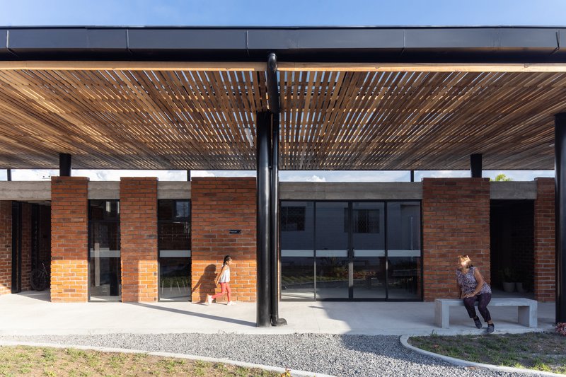 Covered porch with slatted timber ceiling, steel columns and two visitors seated on concrete bench
