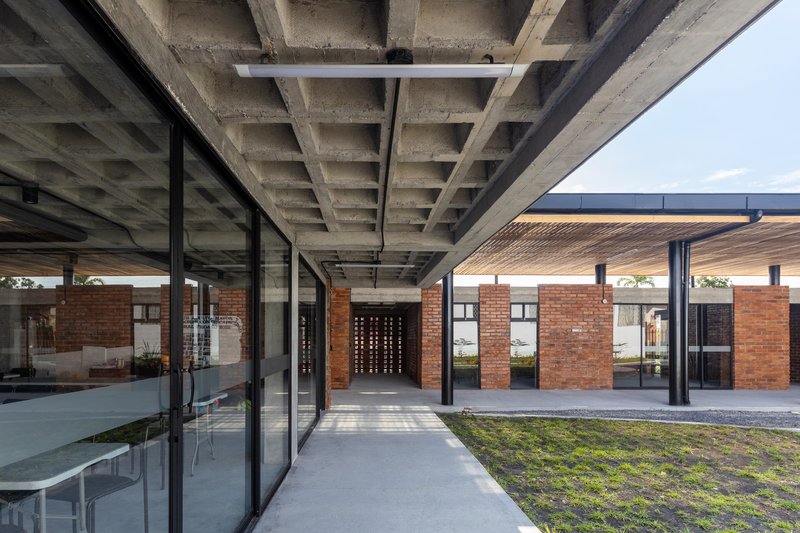 Interior passage with exposed concrete waffle slab above glazed walls opening onto a timber-roofed courtyard beyond