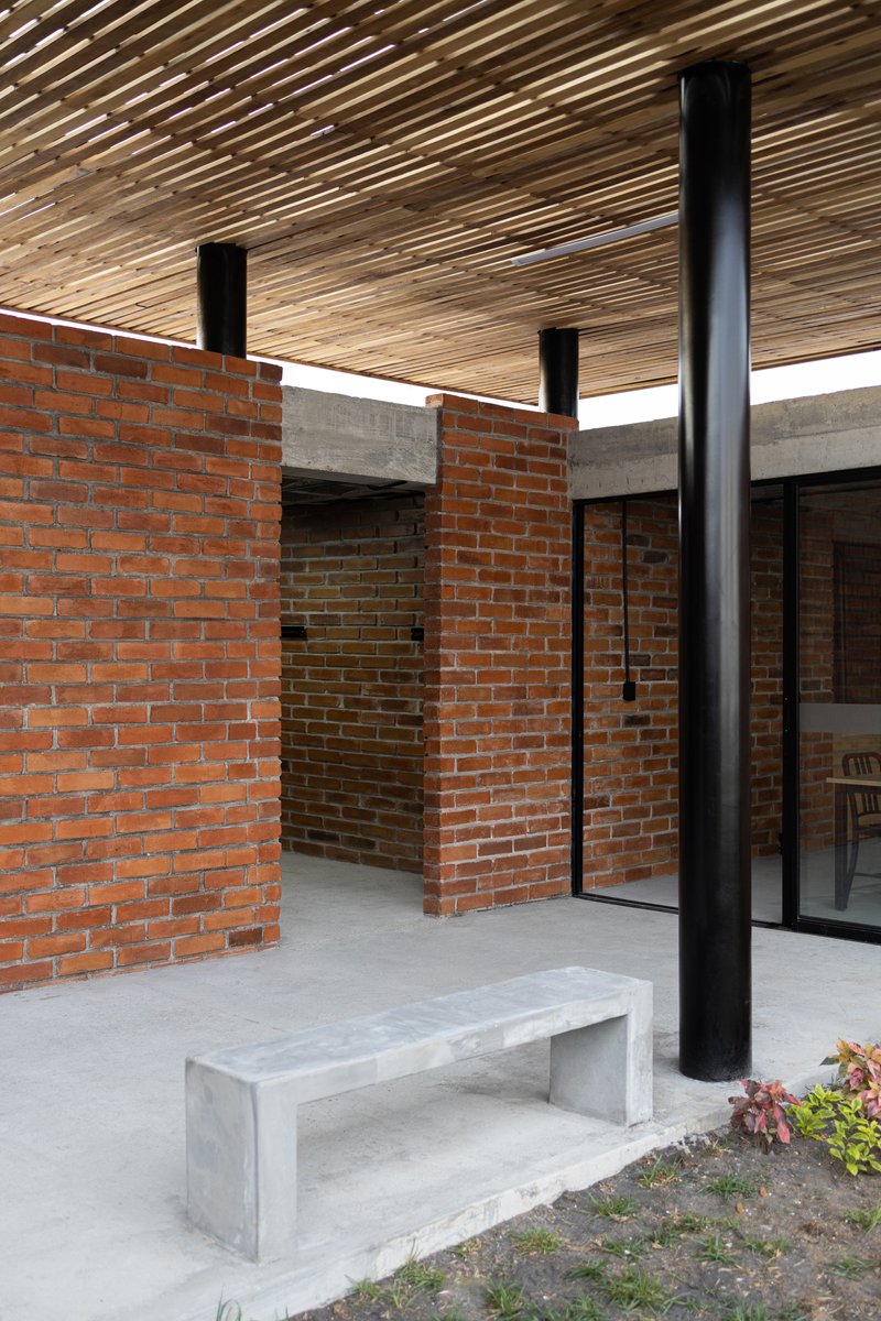 Courtyard space with red brick walls, concrete lintel, and timber slat canopy supported by black columns