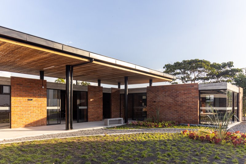 Entry pavilion with extended timber slat roof, steel columns, brick walls, and planted beds at dusk