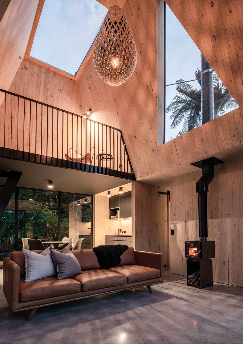 Double-height living space with timber walls, skylight and hanging woven pendant at dusk