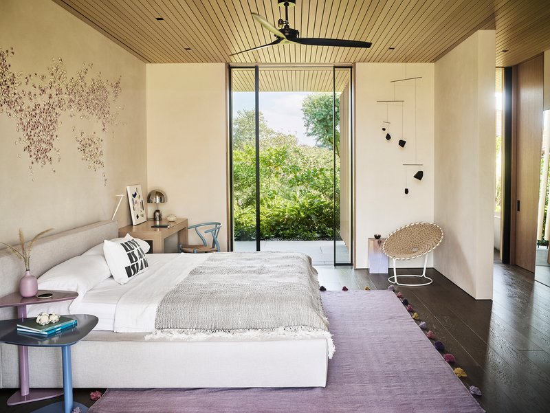 Bedroom with tall glazed door framing view of trees and slatted wood ceiling overhead