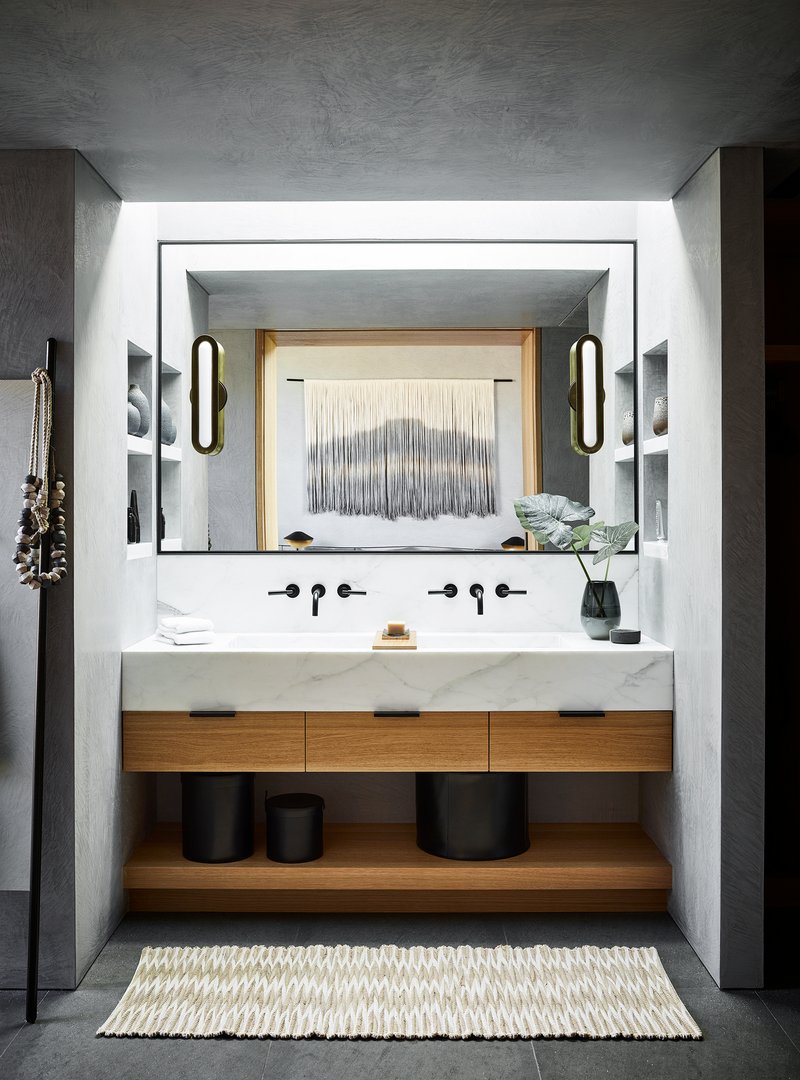Bathroom vanity with floating stone counter, timber drawers, and oval sconces flanking recessed mirror