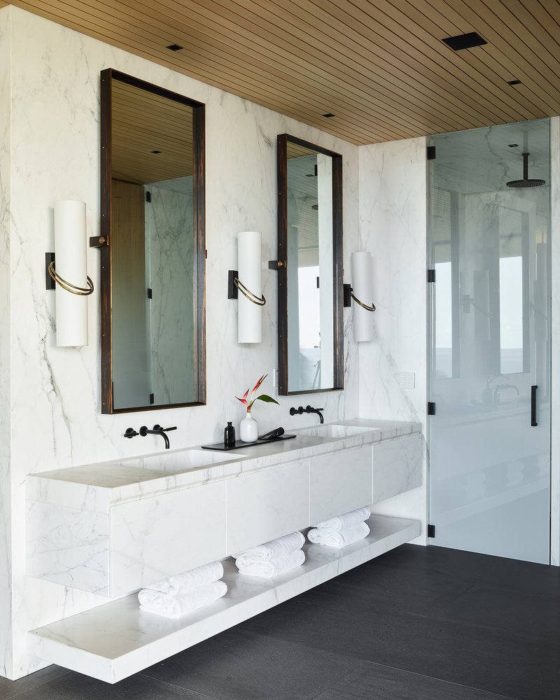 Marble-clad bathroom with twin mirrors, glass-enclosed shower, and slatted timber ceiling