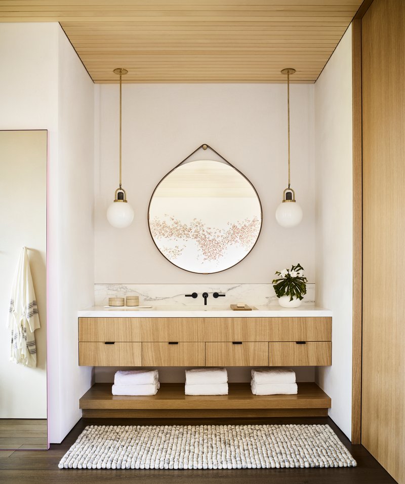 Powder room vanity with timber drawer fronts, circular hanging mirror, and paired pendant lights