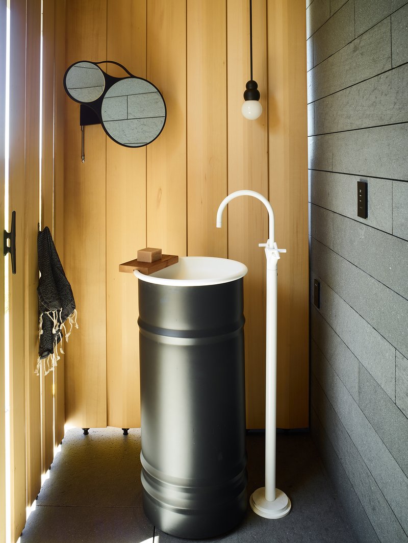 Powder room with cylindrical pedestal sink, vertical timber paneling, and overlapping circular mirrors