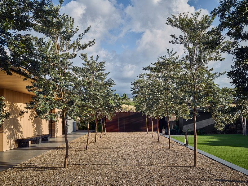 Gravel courtyard lined with trees flanked by low wings under dramatic cloud cover