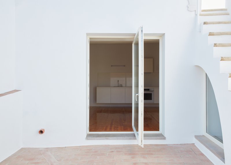 Open glazed door framing a view into the kitchen with terracotta tile flooring