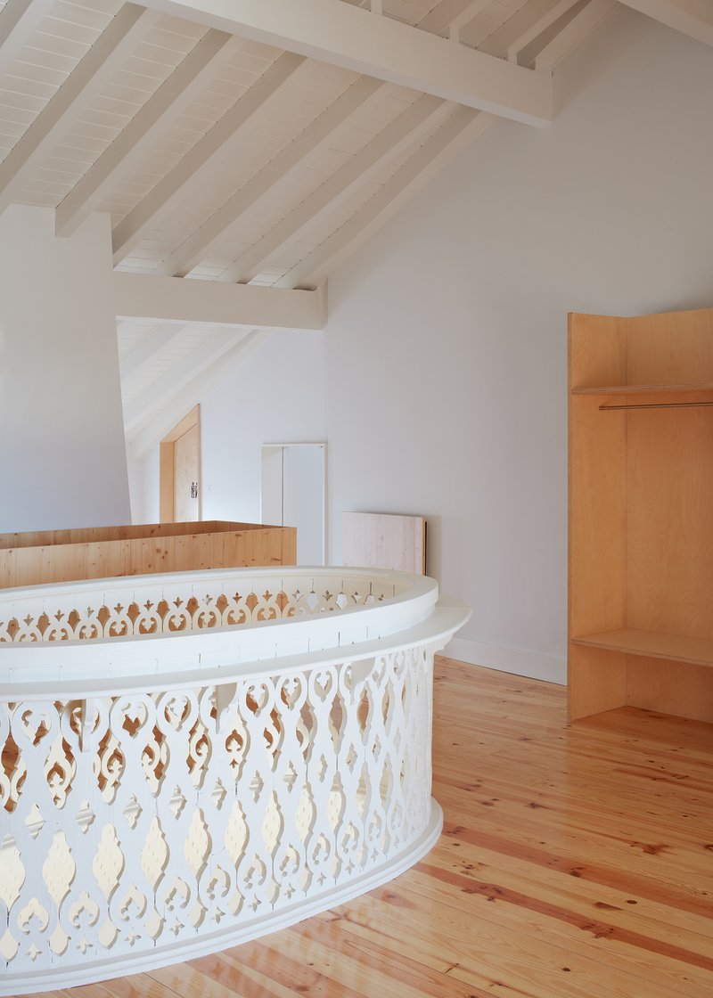 Curved white balustrade with decorative cutouts beside timber joinery under rafters