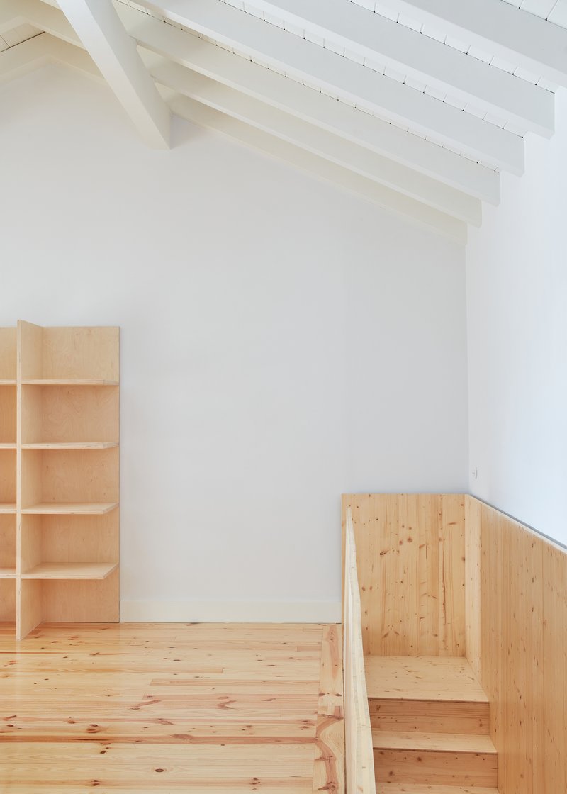 Timber shelving unit and built-in seating beside a stair under painted rafters