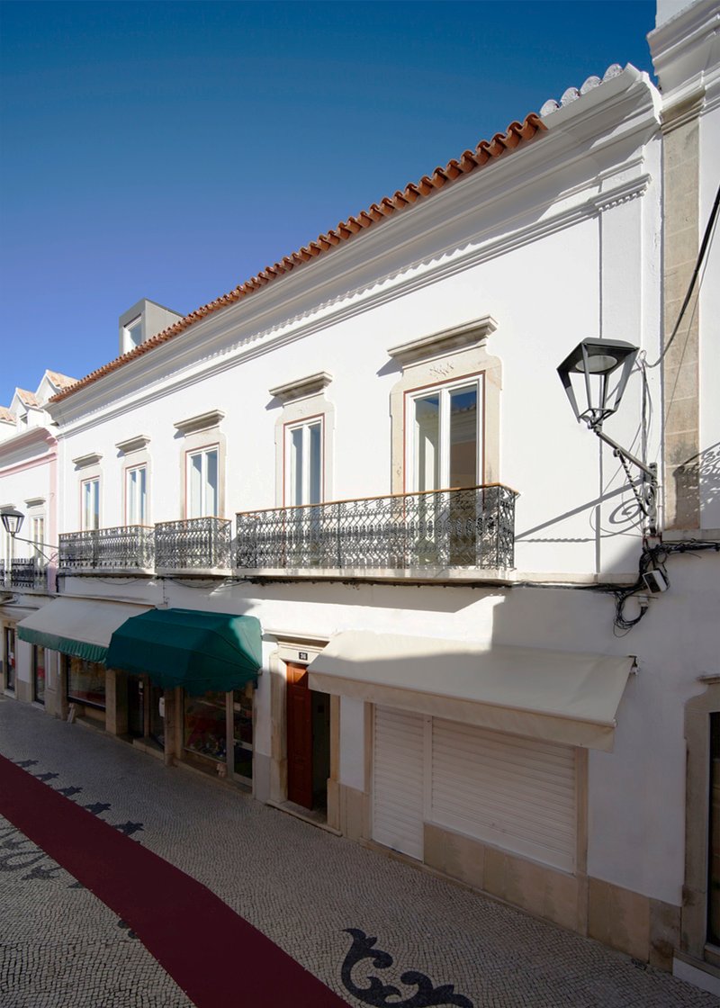Street view of white stucco facade with wrought iron balcony and terracotta tile roof under clear blue sky