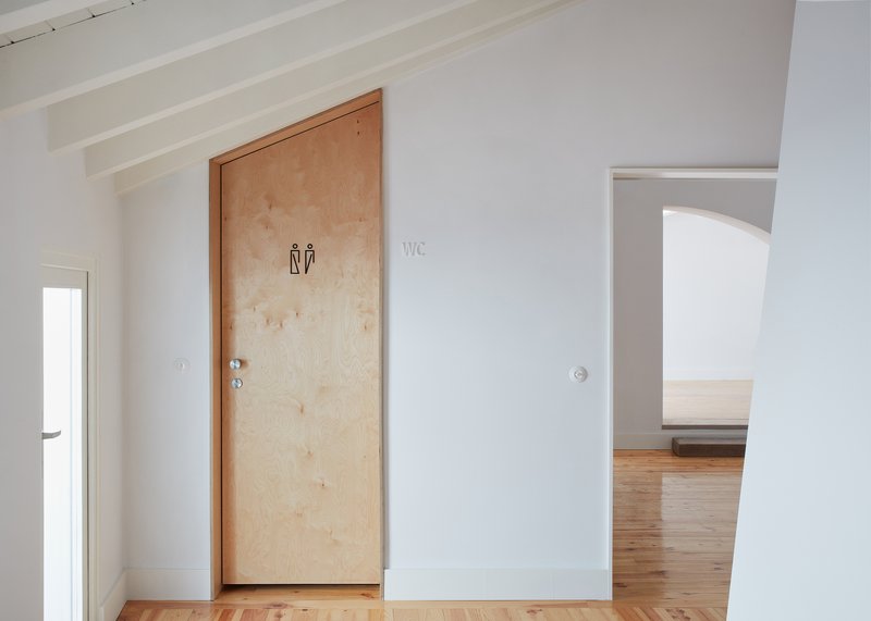 Plywood restroom door with pictogram signage set in white painted walls with exposed ceiling beams