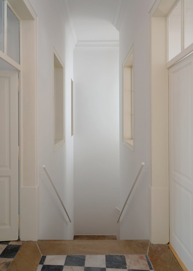 White corridor with vertical niches flanking walls and handrails leading to wooden step